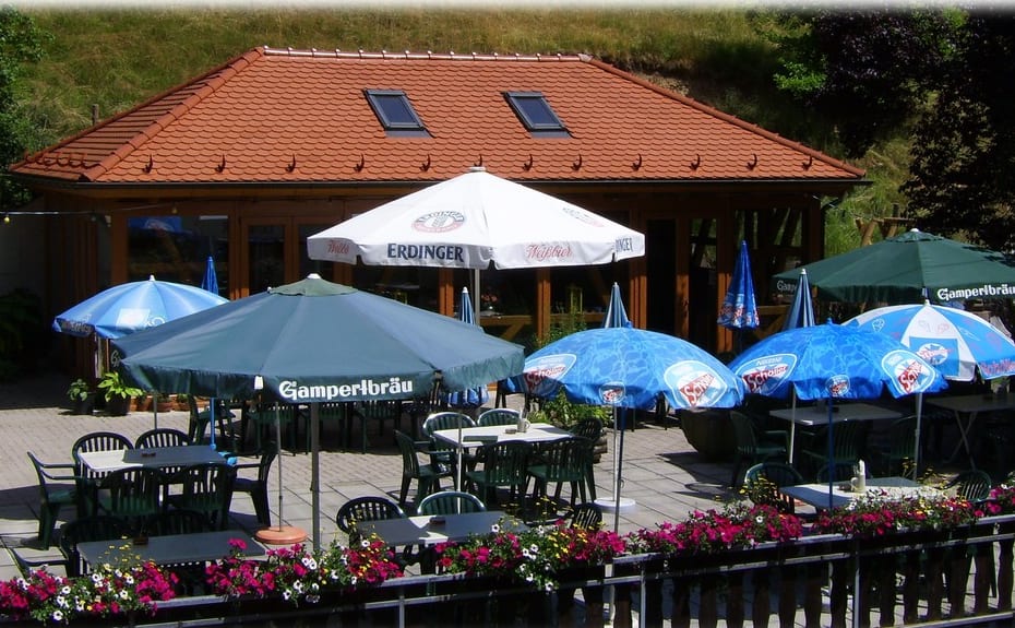 Sonniger Biergarten der Entenmühle mit Grillhaus, Sonnenschirmen und Blumen